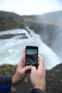 Midsection of man photographing waterfall through smart phone