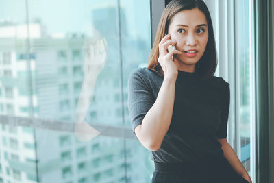 Woman talking on phone while standing by window