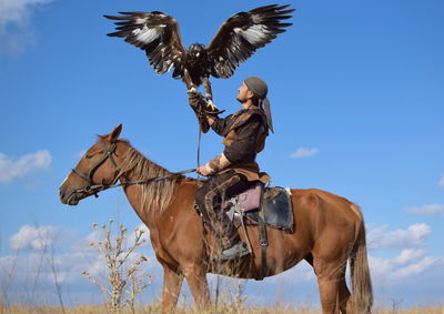 Low angle view of man with golden eagle sitting on horse