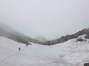 Hikers walking on snowcapped mountain during foggy weather