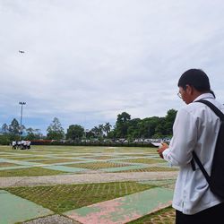 Side view of young man standing on field against sky