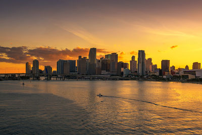Sea by buildings against sky during sunset
