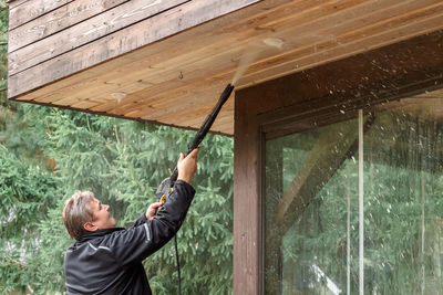 Man cleaning walls and floor with high pressure power washer. washing terrace wood planks and claddi