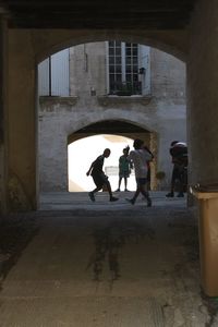 Friends playing soccer by building seen through arch