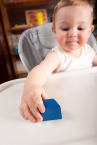 Cute baby boy playing with toy block on high chair