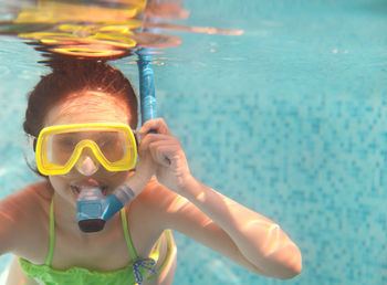 Teenage girl with swimming goggles swimming under water