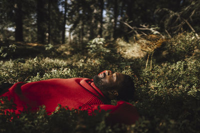 Man sleeping while relaxing on plants in forest