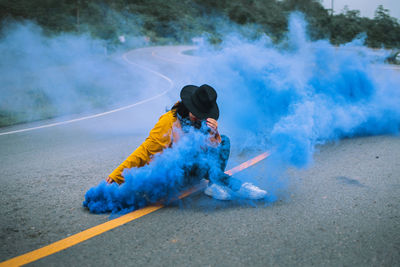 Woman sitting with blue distress flare on road