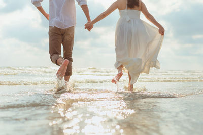 Rear view of couple holding hands while running on beach