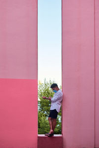 Young man with a mask stands in a pink building