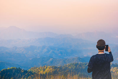 Rear view of man looking and selfie take photo at mountains against sky