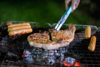 Close-up of hand holding meat on barbecue grill