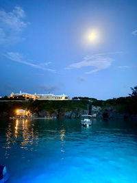 Scenic view of sea by illuminated buildings against sky