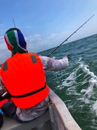 Rear view of man fishing in sea against sky