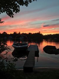 Boats moored at lakeshore against sky during sunset