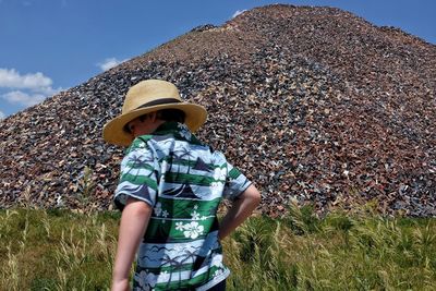 Low angle view of boy in hat standing against bricks on sunny day