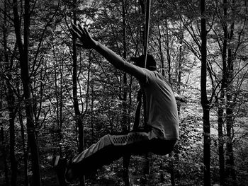 Side view of man climbing on tree trunk in forest