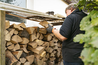 A 50 year old man has received a delivery of firewood and is putting the beech logs into the rack. 