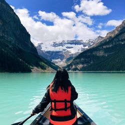 Rear view of woman on lake by mountain against sky