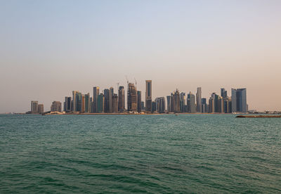 Sea by modern buildings against clear sky