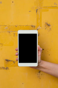 Hand holding smart phone against yellow wall