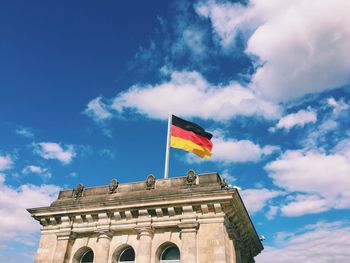 Low angle view of german flag on the reichstag against cloudy blue sky during sunny day