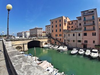 Boats moored on canal by buildings in city against sky