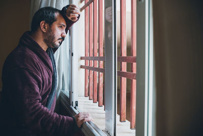 Side view of man standing by window at home