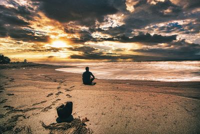 Silhouette woman sitting on beach against sky during sunset