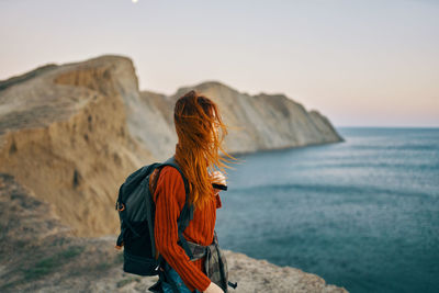 Rear view of person standing on rock against sea