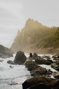 Full length of woman sitting on rock by sea