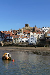 Boats in river by buildings against clear sky