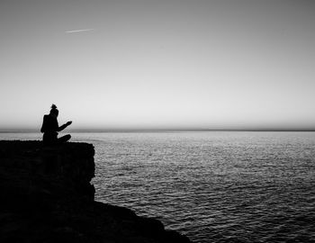 Woman sitting on cliff over sea against sky