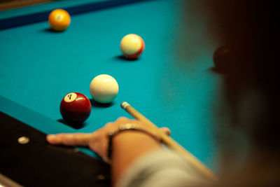 Crop focused bearded male hitting ball with cue while playing game in billiard pool