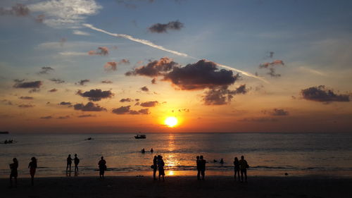 People enjoying at beach against sky during sunset