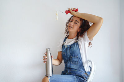 Young woman looking away while sitting against wall