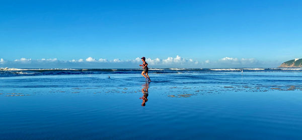 Rear view of woman standing on sea against blue sky