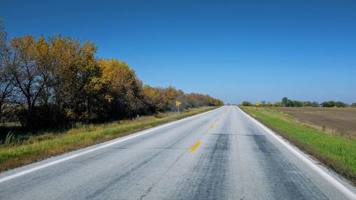 Road amidst trees against clear blue sky