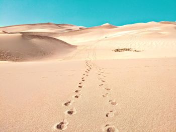 Footprints on sand dune in desert against clear sky