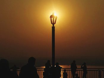 Silhouette people standing on street light against orange sky