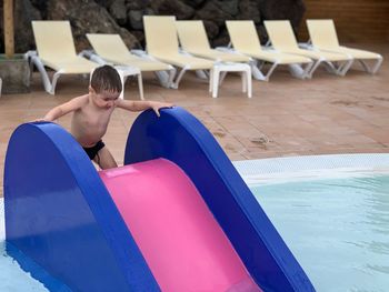 High angle view of shirtless boy sliding in swimming pool