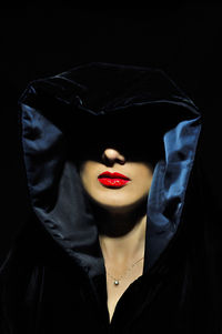 Close-up of woman wearing hooded shirt against black background