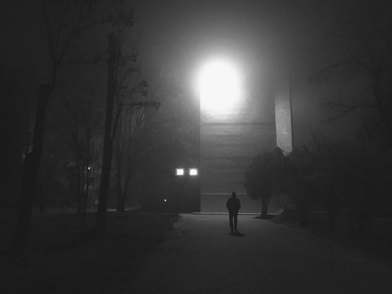 SILHOUETTE PERSON WALKING ON ILLUMINATED STREET AMIDST BUILDINGS