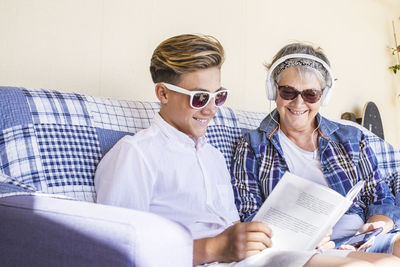 Grandmother with grandson reading book while sitting on sofa at home