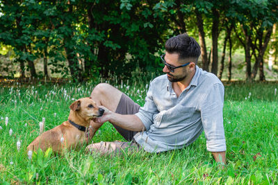 Handsome man is sitting on grass with his dog in park. concept of human and pet relationship.