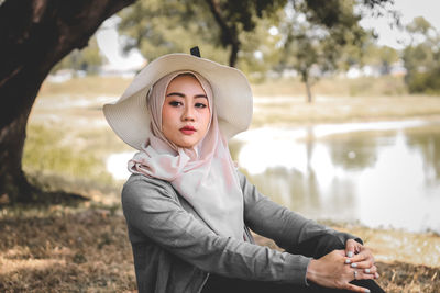 Side view of woman wearing hat while sitting on field