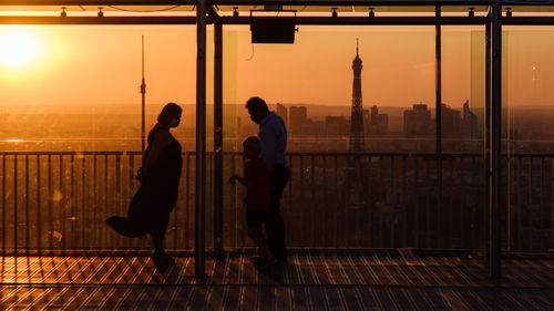 Silhouette people standing by window during sunset