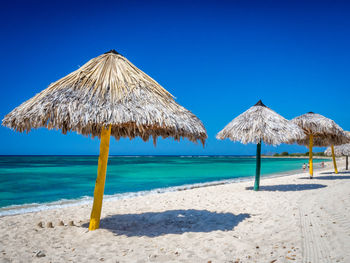 Thatched roof parasol at sea shore against clear blue sky