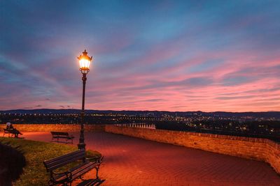 Illuminated street light by river against sky at sunset