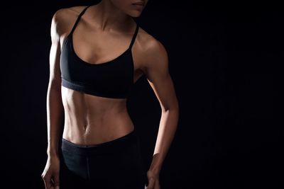 Midsection of female athlete standing against black background